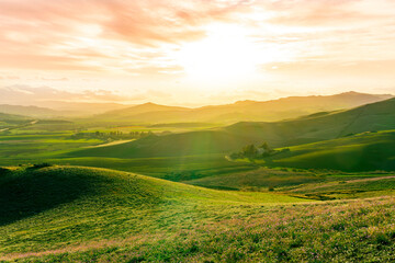 Obraz premium beautiful green valley with green fields with green spring grass with nive hills and mountains and scrnic colorful cloudy sunset on background of landscape