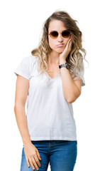 Beautiful young blonde woman wearing sunglasses over isolated background thinking looking tired and bored with depression problems with crossed arms.