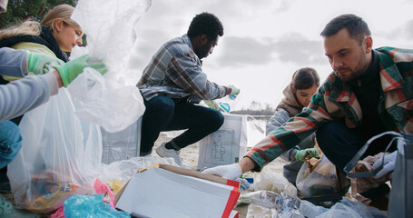 Group of volunteers sorting out collected trash from pile of garbage at beach. Camera moving closer...