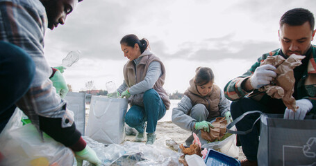Camera moving closer to group of people sorting out collected trash on ground. Placing everything...