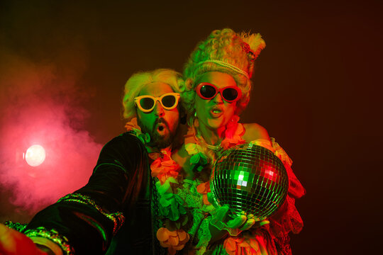 Elegant couple in vintage costumes posing at a vibrant themed party with neon lights