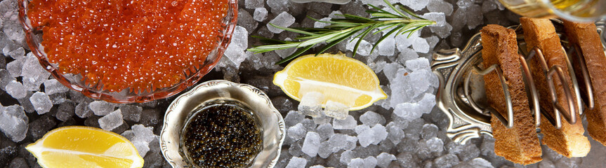 Natural black and red caviar on table. Caviar in transparent dish lies on ice. Ice is scattered on...