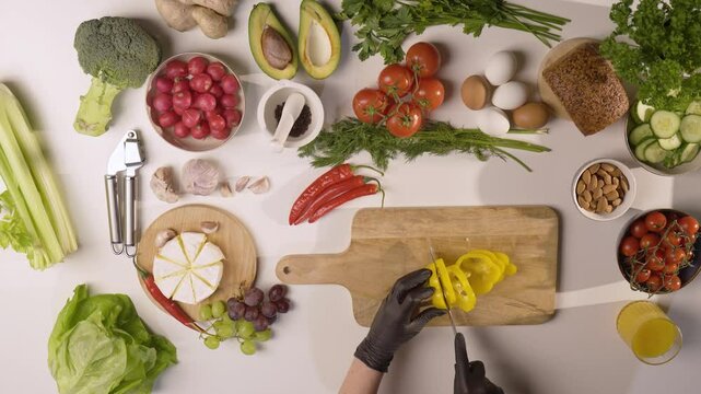Widok z g&oacute;ry na biały st&oacute;ł kuchenny podczas krojenia ż&oacute;łtej papryki w otoczeniu świeżych warzyw, owoc&oacute;w i zdrowych produkt&oacute;w spożywczych