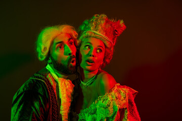 Elegant couple in vintage masquerade outfits illuminated by dramatic lighting on a dark background