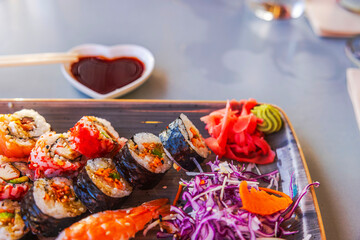 Assorted sushi rolls with pickled ginger, wasabi and soy sauce served on wooden platter in vibrant presentation. Curacao.