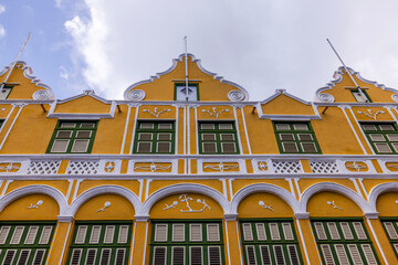 Historic yellow Dutch colonial building facade with green shutters in Willemstad, Curacao.