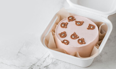Little birthday bento cake with pink cream cheese frosting in a gift box decorated with cute cream teddy bear faces. Birthday cake for a girl on the white marble background