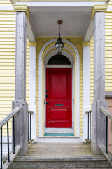 The exterior of a bright yellow house with white trim. There's a vibrant red door with wooden steps...