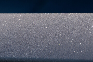 Fototapeta premium A metal railing covered in a small textured pattern of frost crystals. The frozen water has formed frosted particles of ice, cool icy crystals of frosted sleet and snowy diamond sparkles.