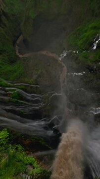 Vertical video. Extreme freestyle flip drone trick tropical island waterfall speed water fall stream rainforest mountain valley aerial view. FPV sport shot jungle cascade fern greenery cliff creek 4k
