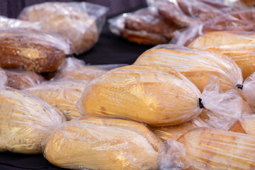 A display of artisan breads in clear plastic bags for sale at a farmer's market. The crusty, sourdough, pumpernickel, white, whole wheat, and traditional homemade rustic loaves are on display for sale