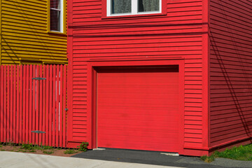 The entrance to a vibrant red wooden two-story residential building. The garage door is a solid...
