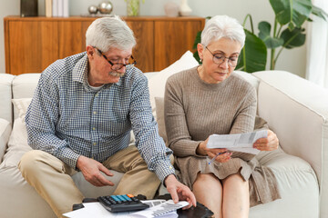 Middle aged senior couple sit with laptop and paper document. Older mature man woman reading paper...