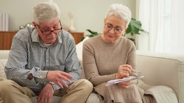 Middle aged senior couple sit with paper document doing financial paperwork. Older mature man woman reading paper bill managing bank finances calculating taxes planning loan debt pension payment
