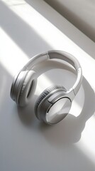 White wireless headphones on white surface with sunlight.