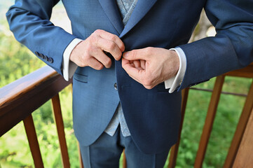 Young handsome stylish man dressed in modern formal clothes buttoning jacket. Close up of hands of guy in blue jacket, violet shirt. 