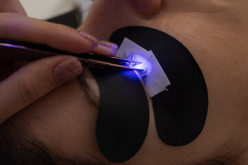 A woman undergoing eyelash extension procedure using an ultraviolet lamp.