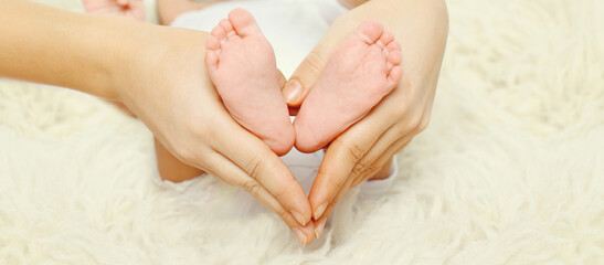 Mother holding in her hands baby feet close up lying on the bed