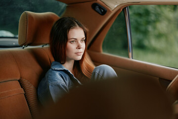 Thoughtful young woman in denim clothing relaxing in the back seat of a car, contemplating life...