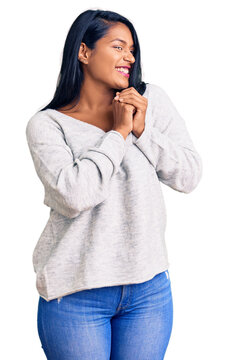 Hispanic woman with long hair wearing casual clothes laughing nervous and excited with hands on chin looking to the side