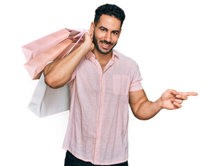 Hispanic man with beard holding shopping bags smiling happy pointing with hand and finger to the...