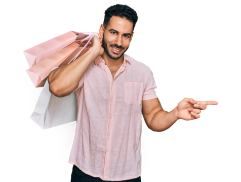 Hispanic man with beard holding shopping bags smiling happy pointing with hand and finger to the side