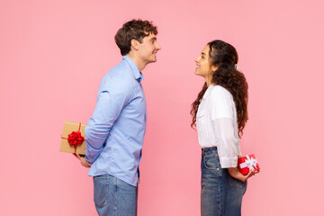 Romantic couple hiding gifts for Valentine's Day or anniversary behind their backs, looking at each...