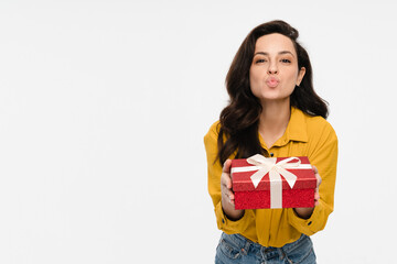 Fototapeta premium Portrait of a happy pretty latin hispanic woman holding giving red present box gift with white ribbon bow sending blowing kiss standing looking at camera isolated over white background