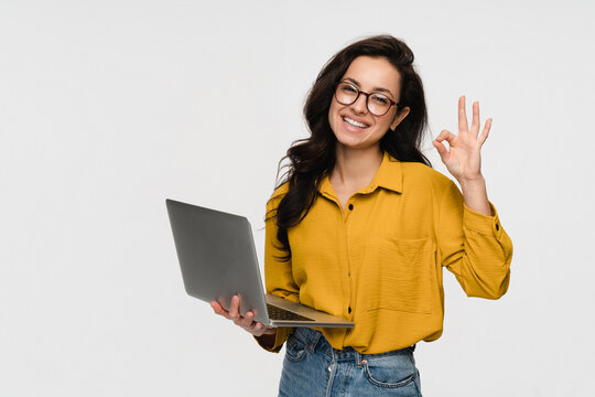 Portrait of young woman student worker using laptop for remote work, e-learning at university college, e-banking, online shopping, webinars showing ok okay sign isolated over white background