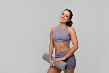 Smiling sporty woman with healthy strong body in tracksuit poses with rolled fitness mat does yoga...