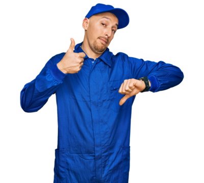 Bald man with beard wearing builder jumpsuit uniform doing thumbs up and down, disagreement and agreement expression. crazy conflict