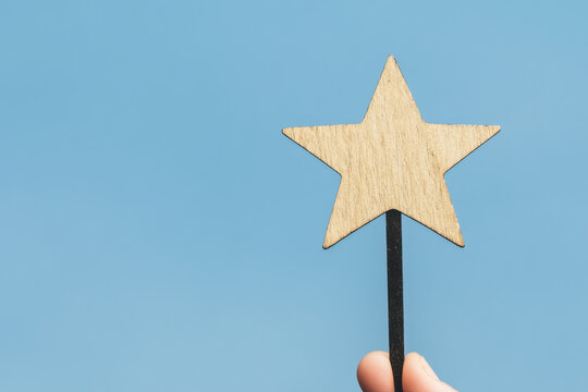 A wooden star is held up in the air with a blue sky in the background