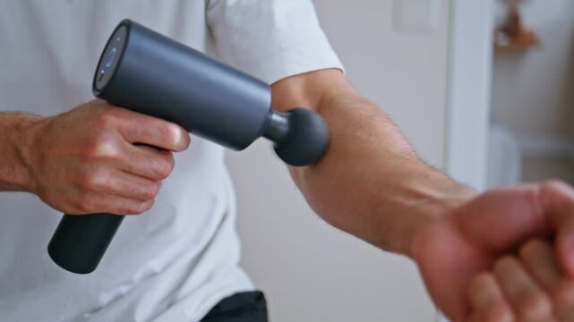 Massage gun massaging arm after sport activity in apartment closeup. Sportsman