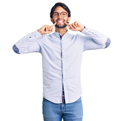 Fototapeta premium Handsome hispanic man wearing business shirt and glasses smiling with open mouth, fingers pointing and forcing cheerful smile