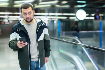 Male passenger in casual clothing talking on his mobile phone next to the subway escalator in subway