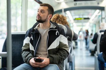 Portrait of european man standing in tram carriage and using his phone