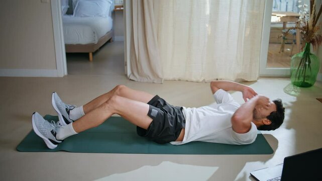 Man pumping abs muscles on sport mat at apartment floor. Athletic guy workout