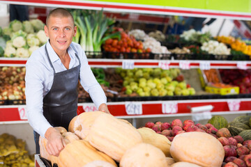 Portrait of smiling successful greengrocery owner laying out fresh fruits and vegetables on counter