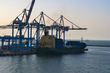 a big green ship is docked in the port with cranes