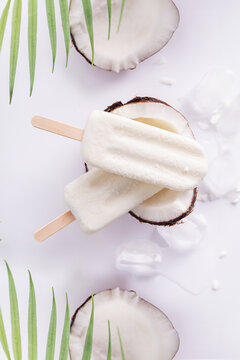 Picol&eacute; sabor coco no fundo branco com peda&ccedil;os de coco e folhas de coqueiros no fundo.