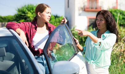 Young woman got out of her car and asking way to destination. She's talking with Asian woman who's...