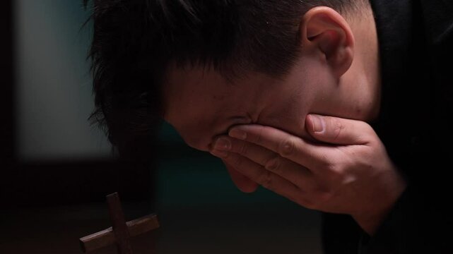 Young man praying and crying in front of cross suffering from depression
