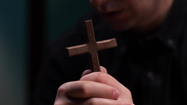 Priest praying and holding wooden cross in hands
