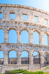 Obraz premium The Roman amphitheatre in Pula stands as a monumental reminder of ancient architecture. Visitors admire its impressive structure under a clear blue sky, showcasing its historical significance.