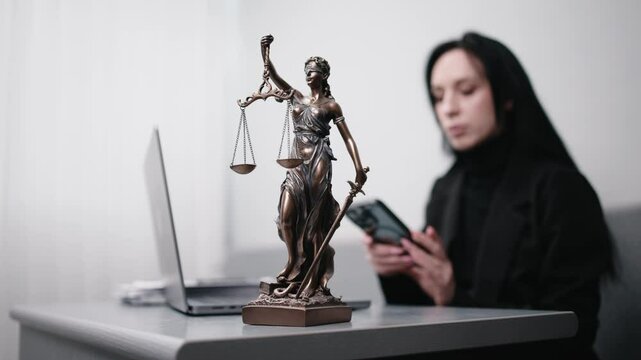 A lawyer works at their desk, sorting papers and entering data on a laptop. The statue of Themis stands nearby. Concept of legal decisions, work, and court proceedings.