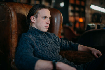 Portrait of a young sullen, sad man in a chair.