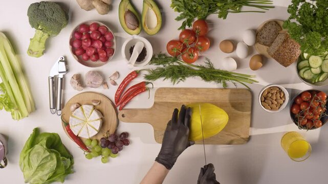 Krojenie ż&oacute;łtego melona na drewnianej desce w otoczeniu świeżych warzyw, owoc&oacute;w i składnik&oacute;w &ndash; zdrowa żywność, kulinarna inspiracja, przygotowanie posiłk&oacute;w w domu