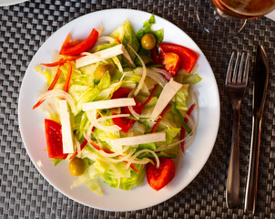 Crisp and refreshing colorful salad, perfect for dinner, with mix of lettuce, sliced tomatoes, onion, olives and cheese, served on white plate..