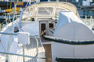 Sailing yacht moored in marina on sunny day showing deck, covered sail, and winch