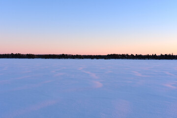 A breathtaking view of the frozen lake, blanketed in snow, with frosted trees stretching across the horizon
